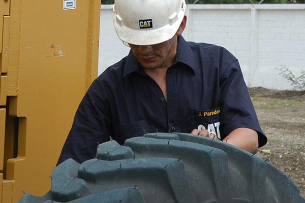 Worker with °ϲʿ¼ shirt and construction helmet inspecting a large tire